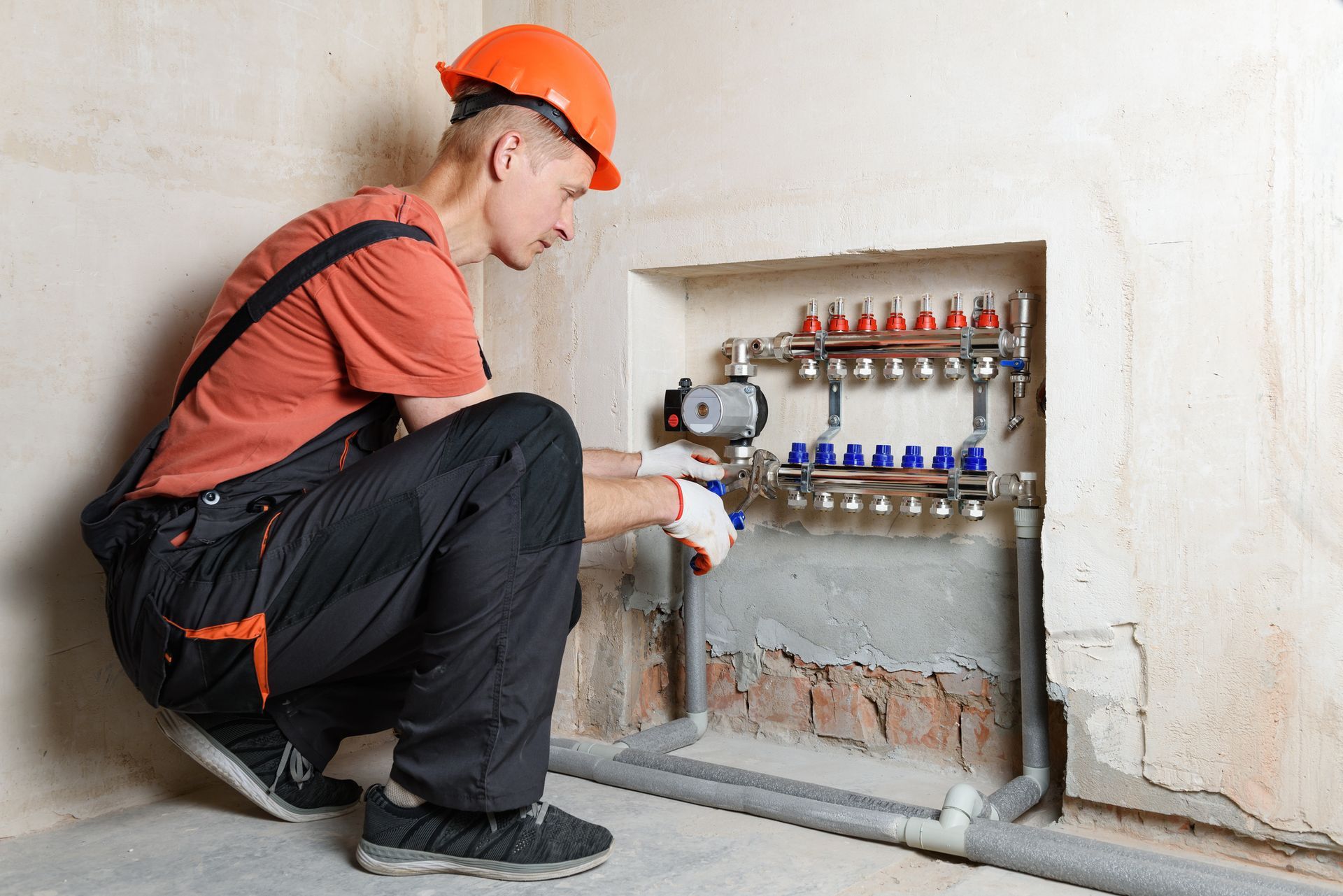The plumber is fixing the distribution manifold to the floor heating system. The plumber is fixing the distribution manifold to the floor heating system.