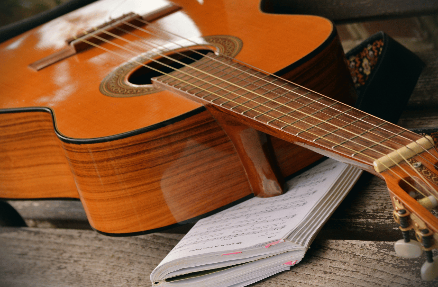 An acoustic guitar rests on top of a notebook on a wooden table