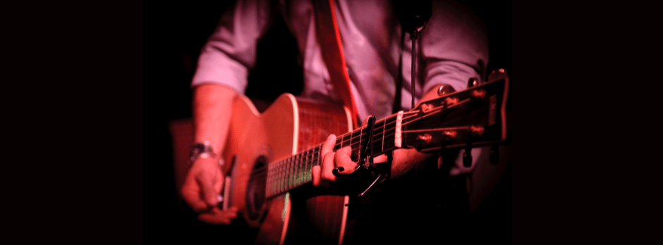 A man is playing an acoustic guitar in a dark room.
