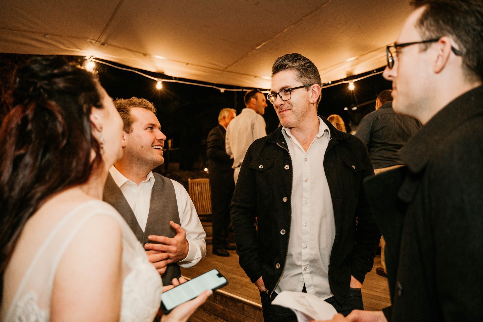 A group of people are standing under a tent talking to each other.