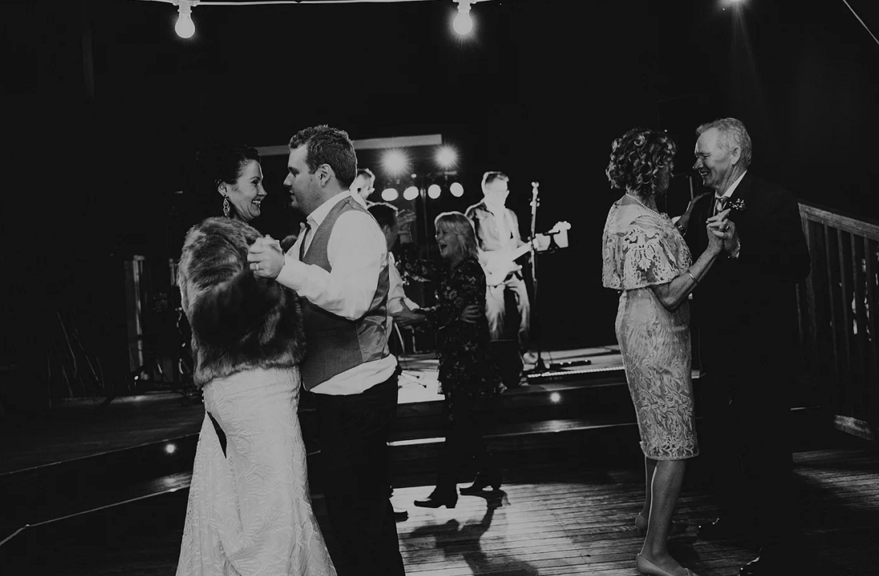 A bride and groom are dancing with their parents at their wedding reception.