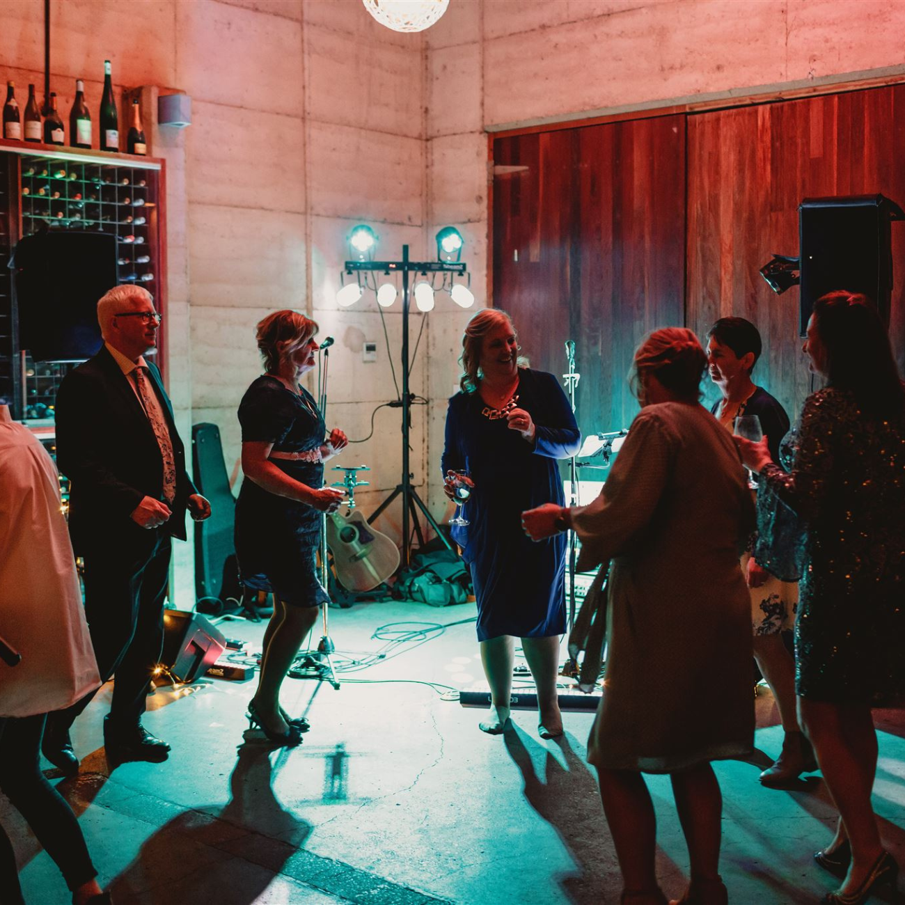 A group of people are dancing in a room with bottles of wine on the wall