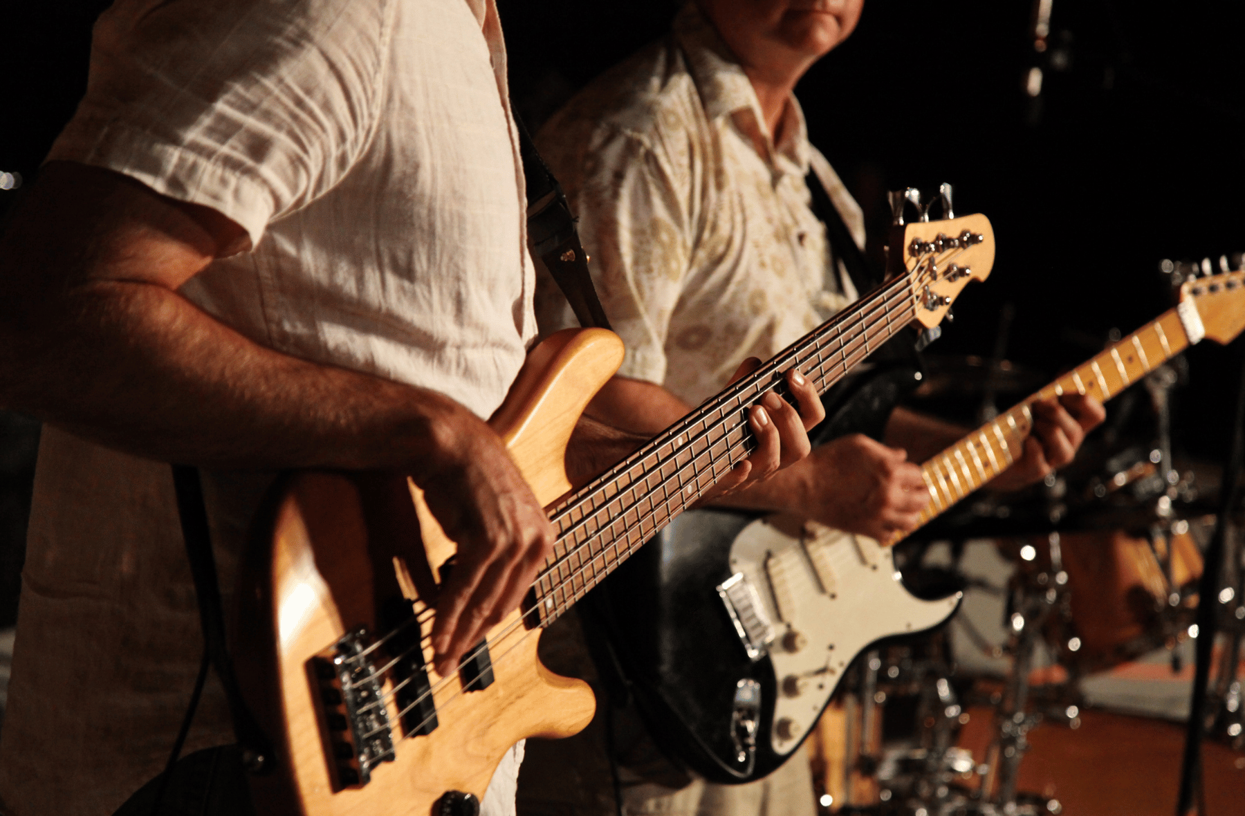 Two men are playing guitars in front of a drum set.