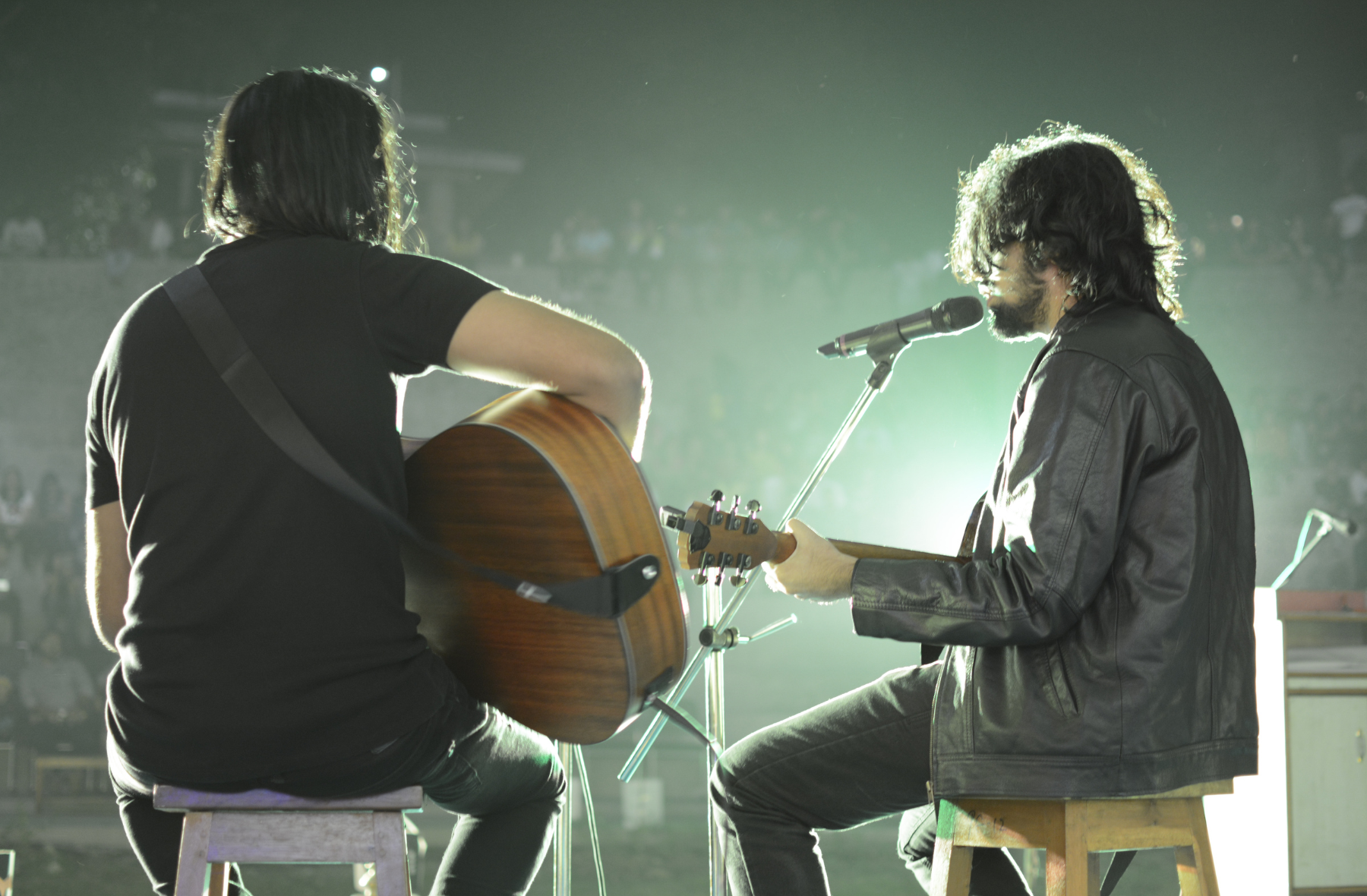 Two men are playing guitars and singing into microphones on a stage