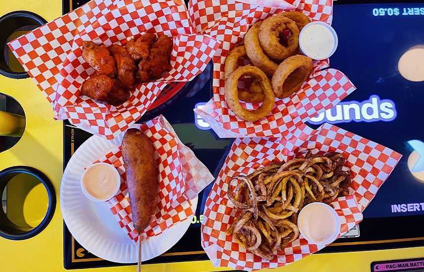 A table topped with plates of food including corn dogs , onion rings , and french fries.