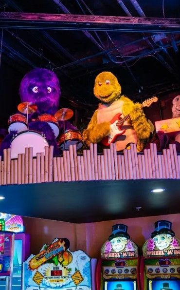 A purple monster is playing drums and a yellow turtle is playing a guitar in an arcade.
