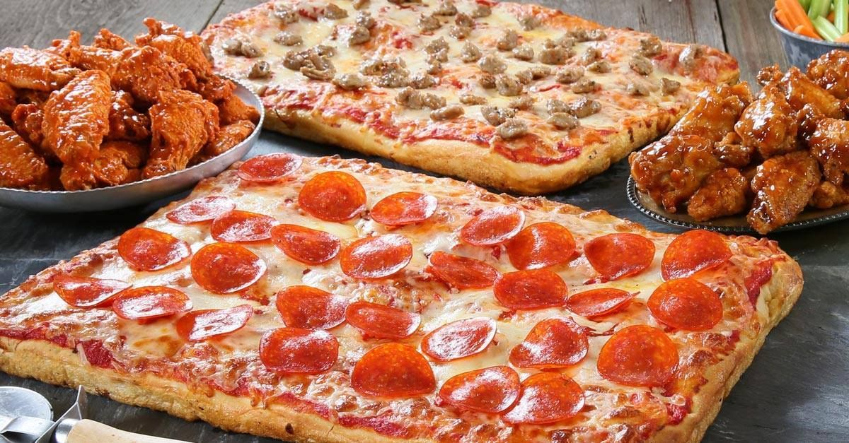 There are many different types of pizzas and wings on the table.