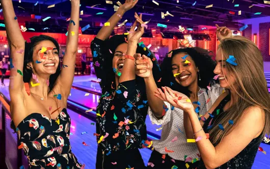 A group of women are standing next to each other at a bowling alley.
