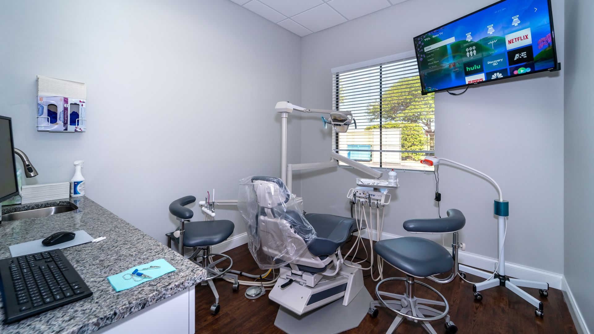 A dental office with a dental chair , desk , computer and television.