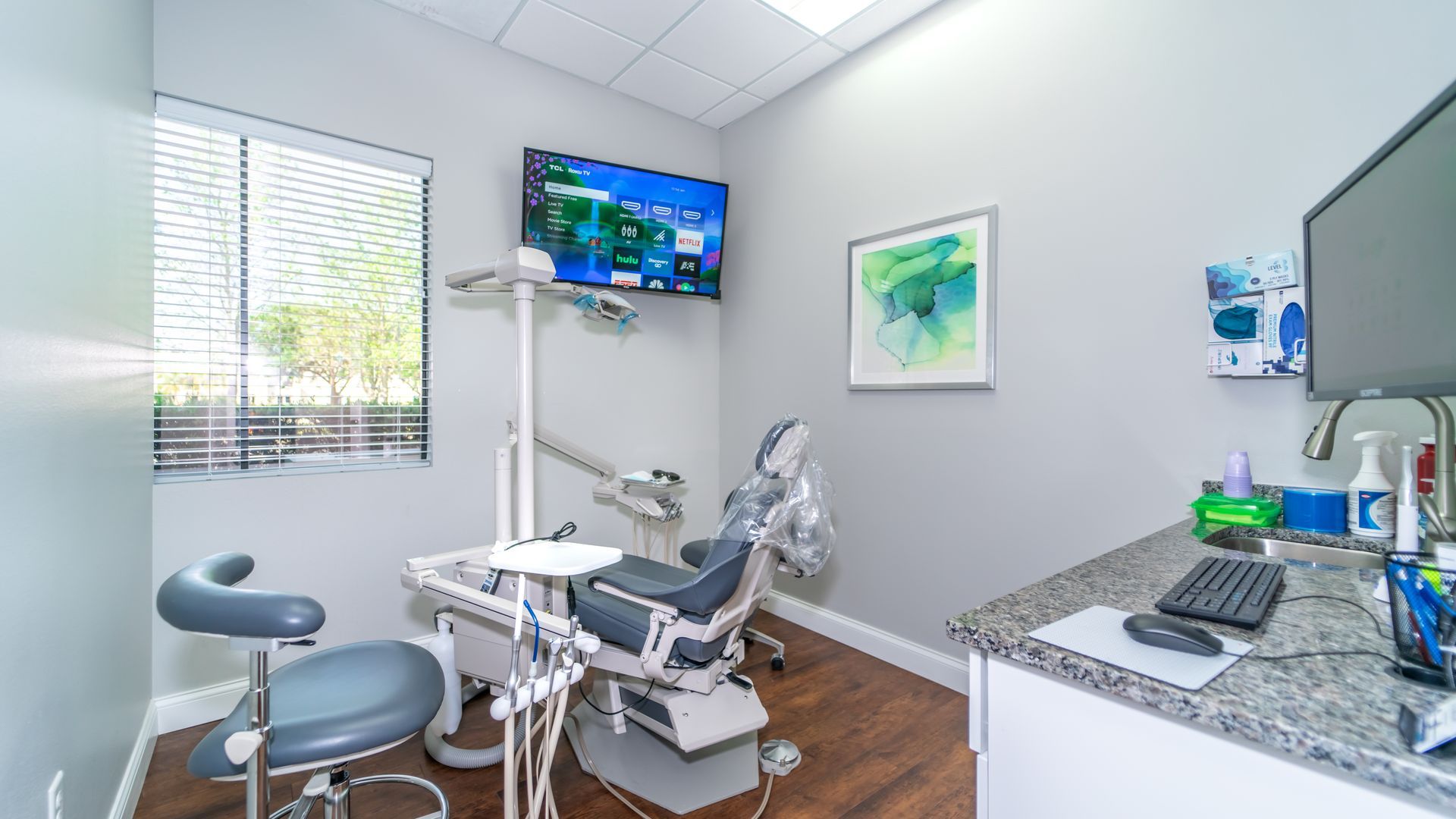 A dental office with a dental chair , desk , computer and television.