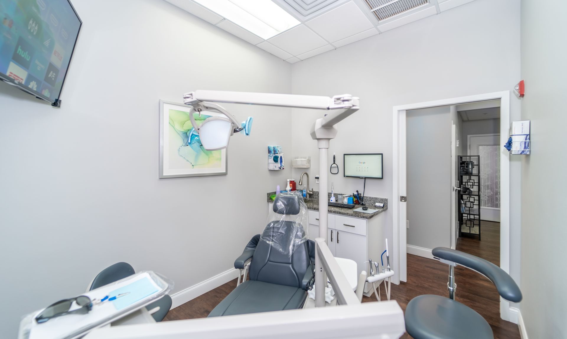 A dental office with a dental chair and a monitor on the wall.