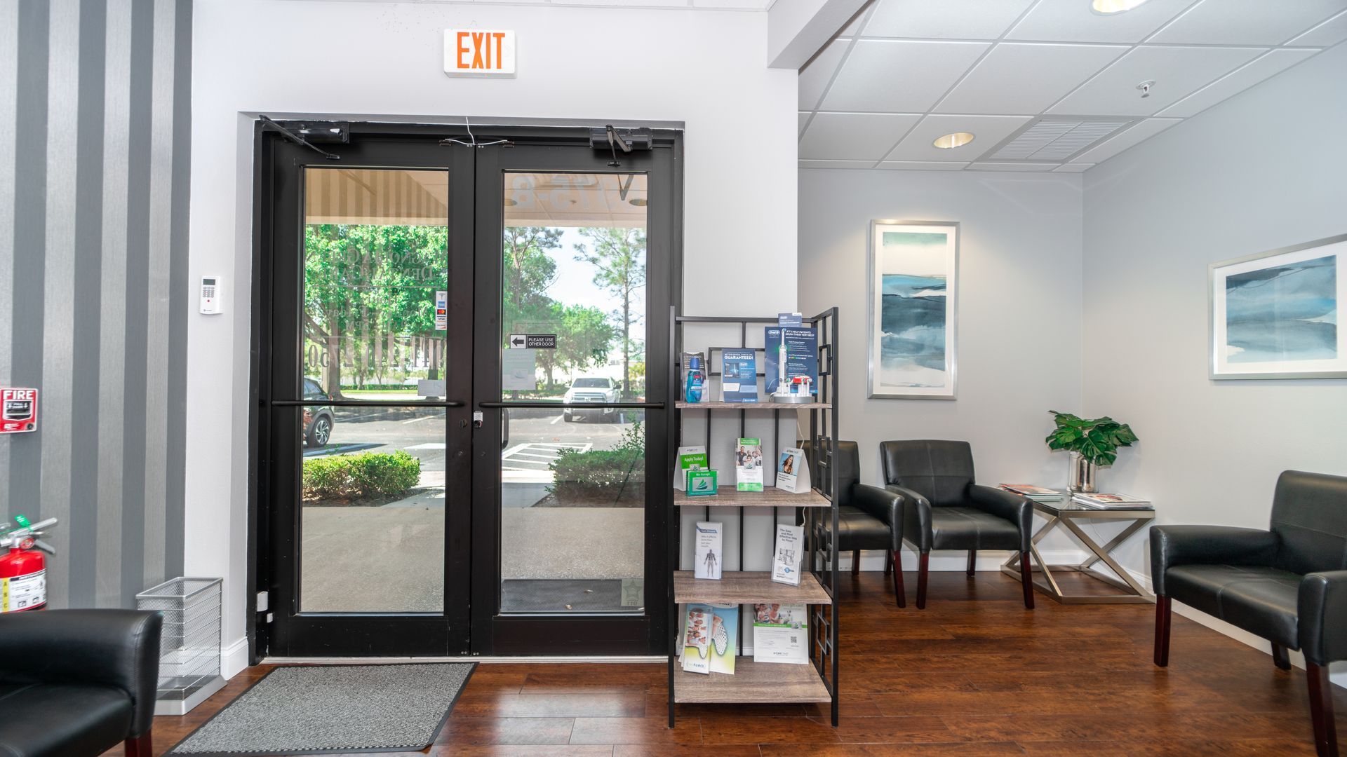 A waiting room with chairs , a bookshelf and an exit sign.