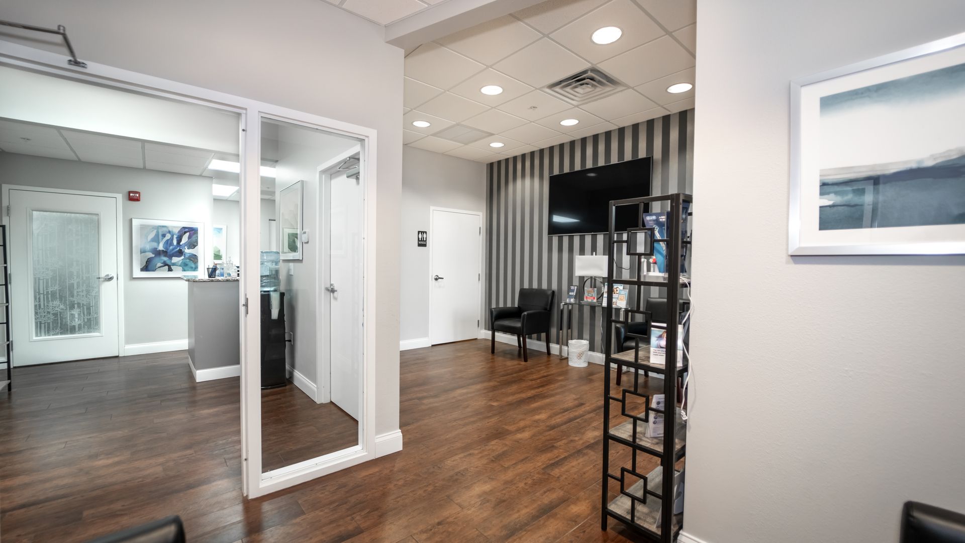 A waiting room with wooden floors and a television on the wall.