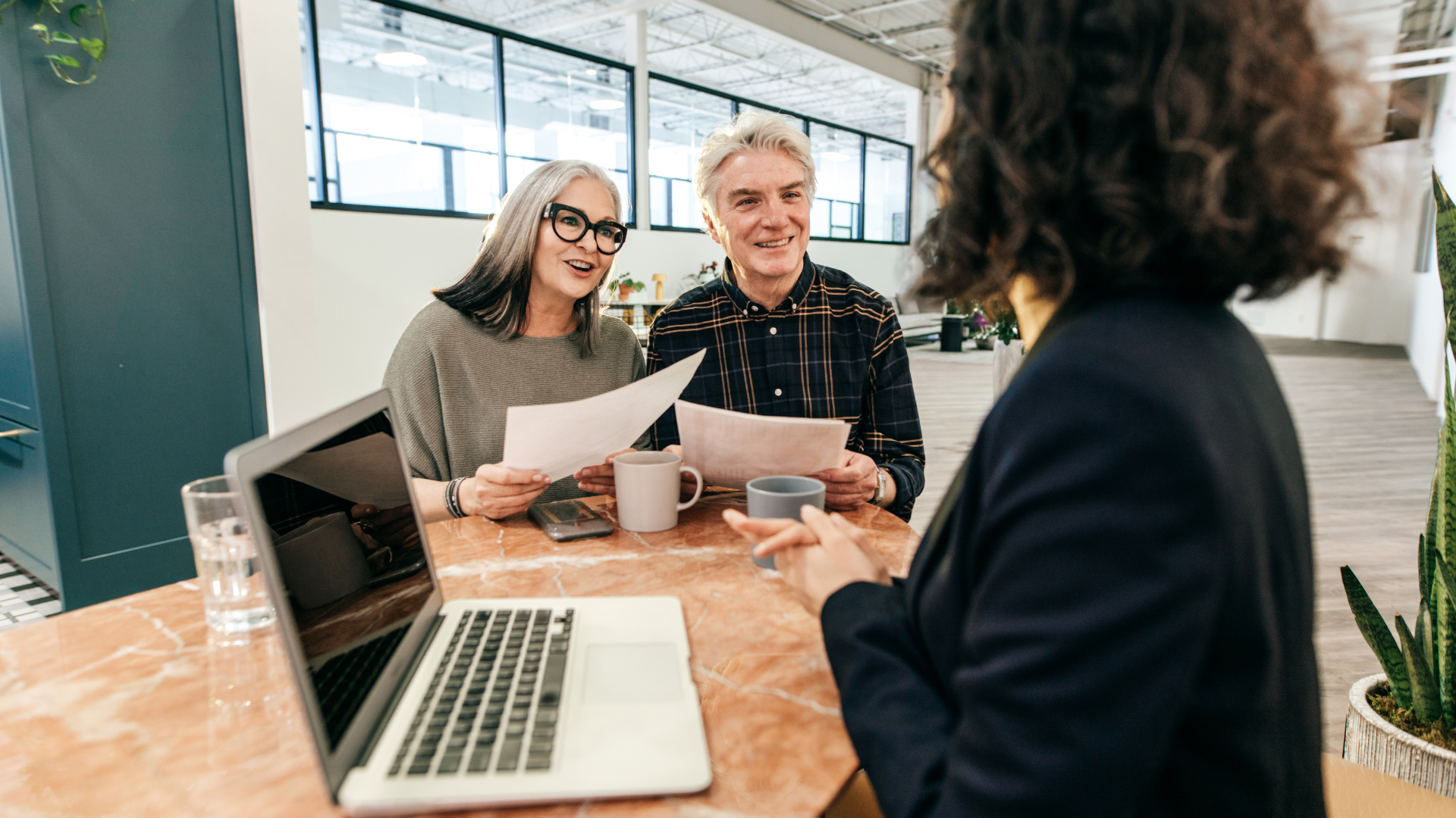 A financial advisor speaks with a couple in a bright office, reviewing papers and using a laptop.