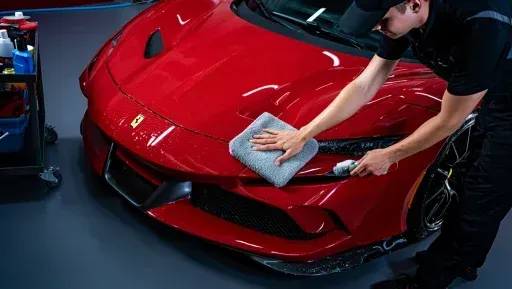 A man is cleaning a red sports car with a towel.
