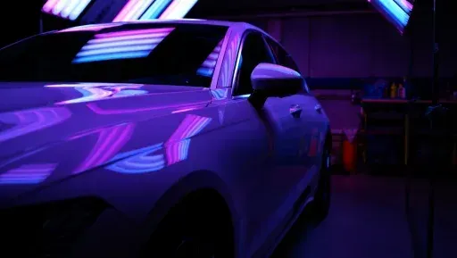 A purple car is parked in a dark garage with neon lights.