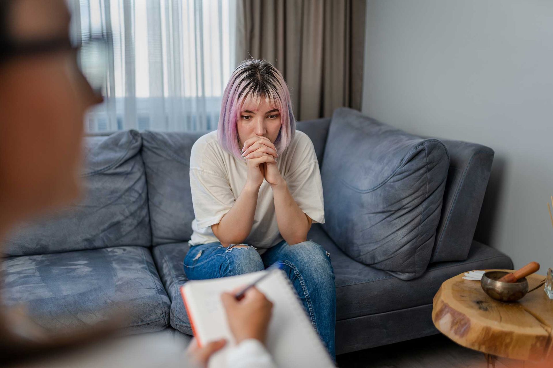 A woman with pink hair is sitting on a couch talking to a doctor.