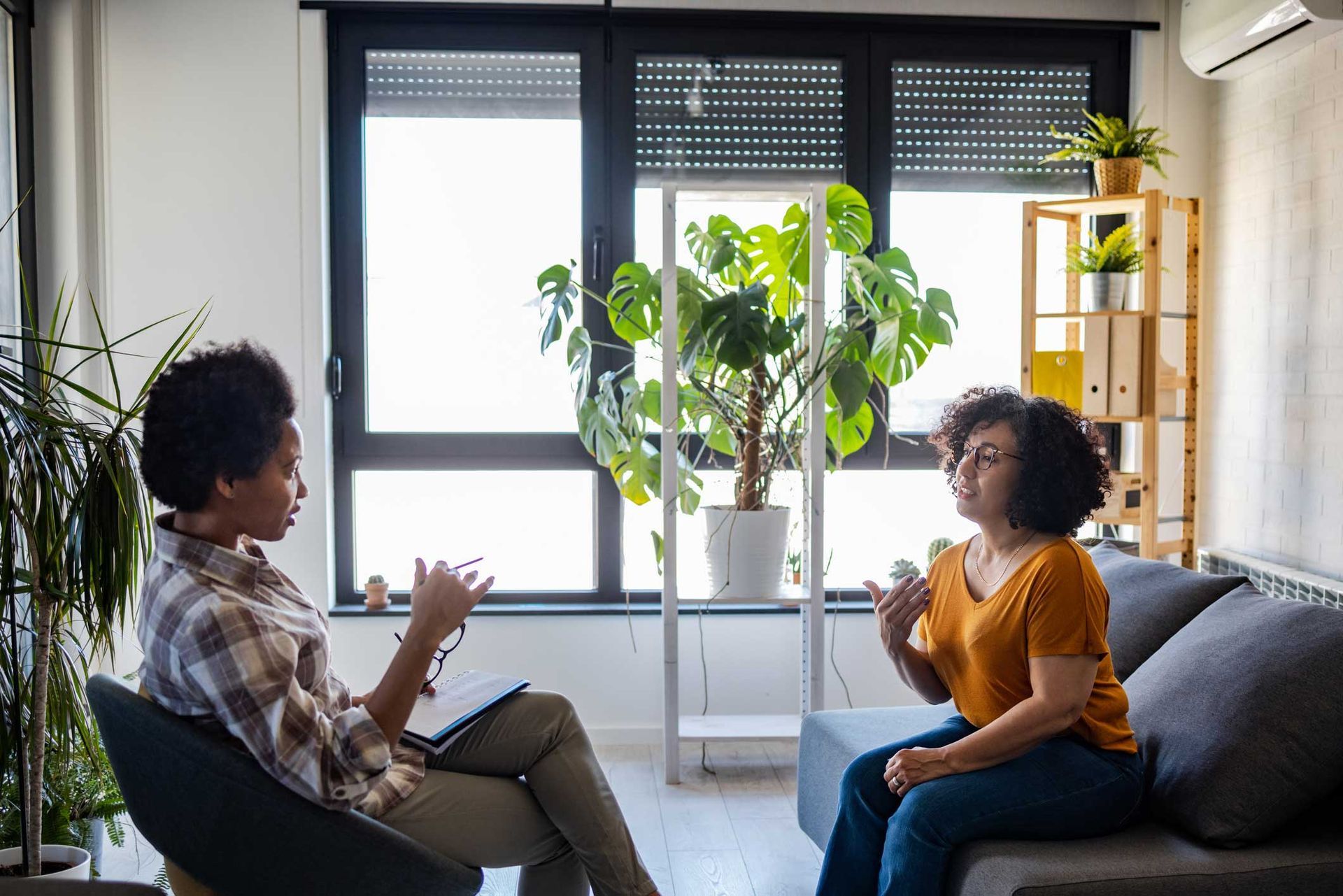 Two women are sitting on a couch talking to each other in a living room.