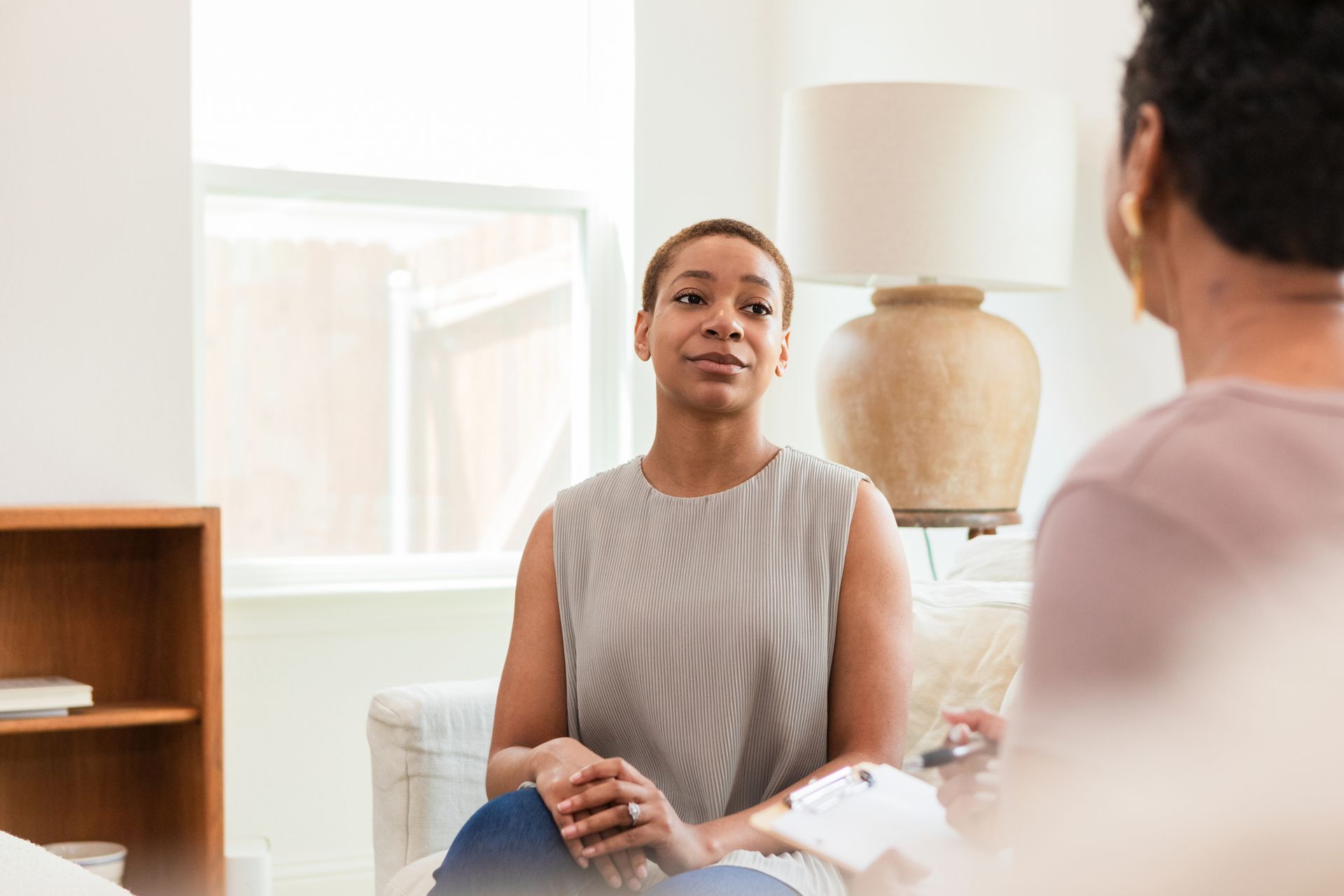 A woman is sitting in a chair talking to a man while holding a clipboard.