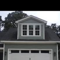 Gray house with white garage door and dormer windows under a cloudy sky.