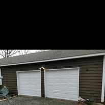 Two white garage doors on a brown-sided building with a dark roof.