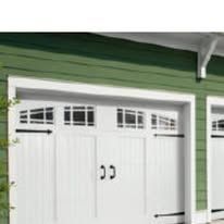 White garage door with rectangular windows, black handles and hinges, green siding.