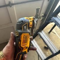 Person holding a black and yellow oscillating multi-tool near a metal structure.