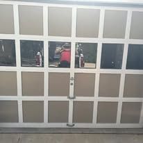 Garage door with multiple rectangular glass panes reflecting a person holding something.