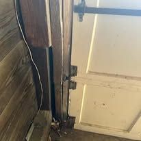 Wooden garage door frame with damage, next to a white door.