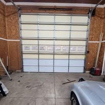 Garage door, partially open. White and blue panels, indoors. Car's front visible.