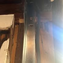 Metal beam against wood beams. Some holes in the metal. Inside a structure.