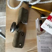 Close-up of a broken door hinge with a wheel, on a wooden surface.