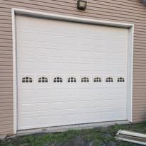 White garage door with small arched windows in a beige building.