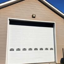 White garage door on tan siding with a small light above.