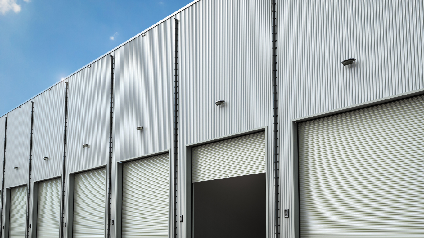 Exterior of a modern building with corrugated metal siding, featuring several garage door openings. Blue sky.