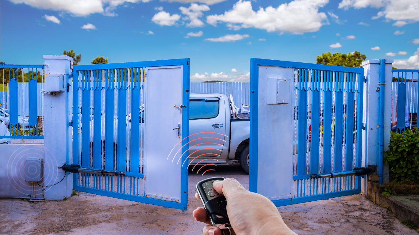 Hand holding a remote opening a blue and white automatic gate, with a truck parked inside.
