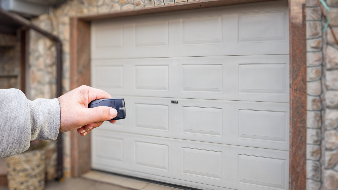 Hand operating a garage door opener remote. Beige garage door in focus.