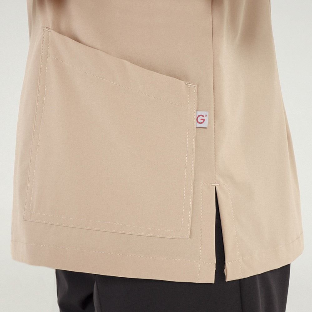 Primo piano di una casacca medica color marrone chiaro con una grande tasca e uno spacco laterale.