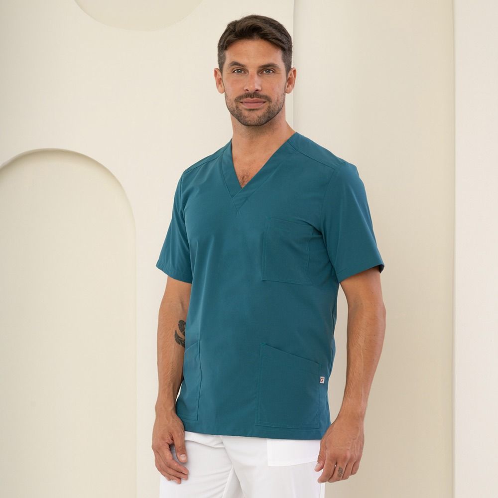 Uomo in camice verde acqua e pantaloni bianchi. In piedi in una stanza ben illuminata.