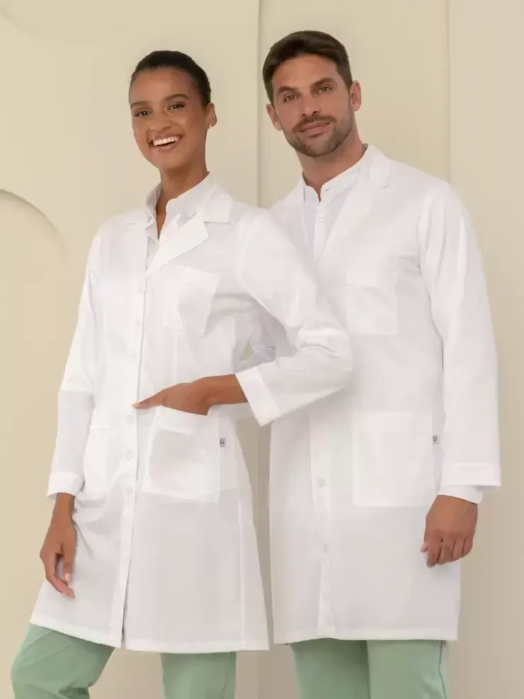 Due persone che indossano camici bianchi e pantaloni verde chiaro, sono in piedi una accanto all'altra e sorridono.