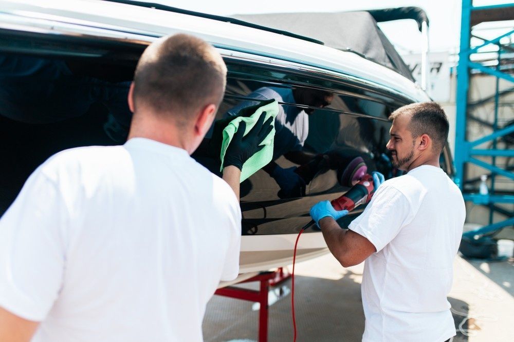 Two People Cleaning a Black Boat Hull; One Uses a Buffer, the Other a Cloth  — Ryders Garage in Erina, NSW
