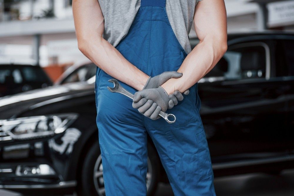 Mechanic in Blue Overalls Holding a Wrench Behind Their Back in A Garage — Ryders Garage in Copacabana, NSW