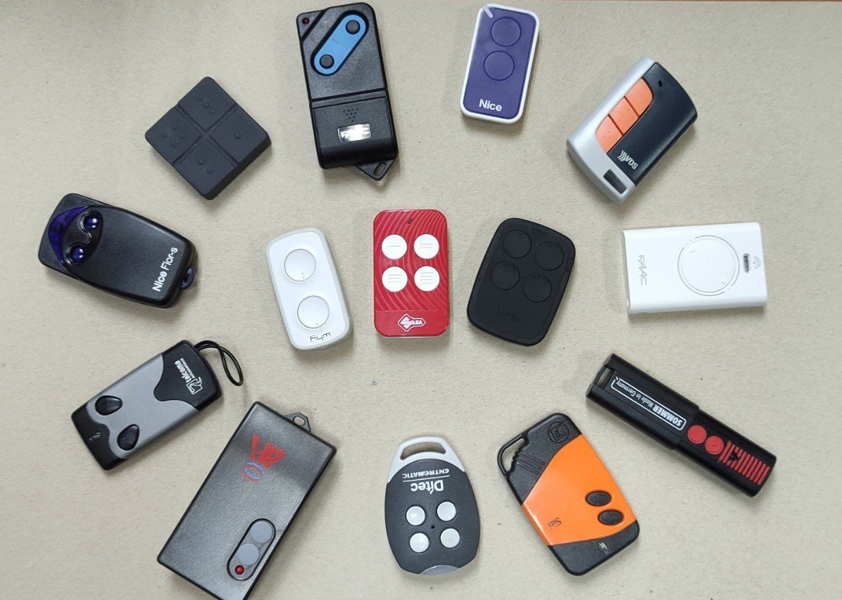 Una collezione di telecomandi per porte da garage di vari colori, disposti in cerchio su una superficie chiara.