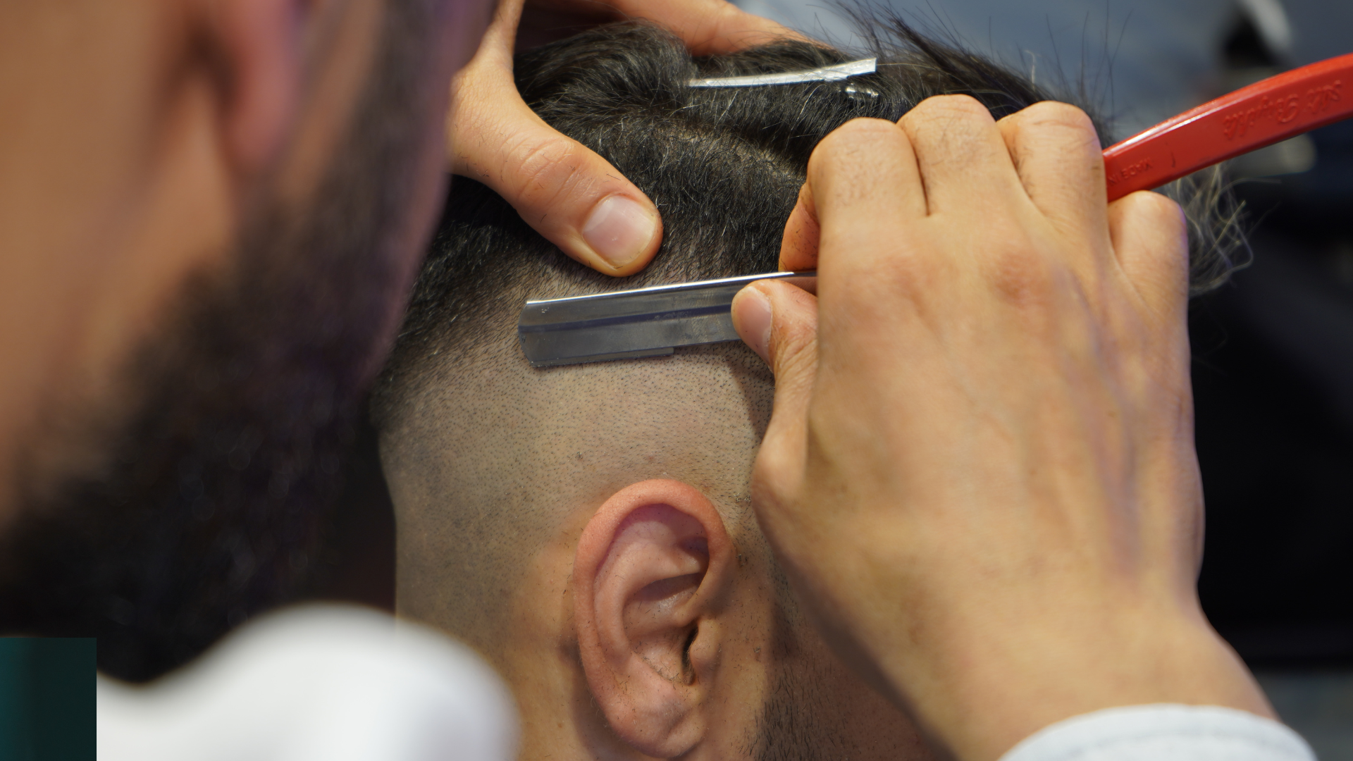A man is getting his hair cut by a barber with a razor.
