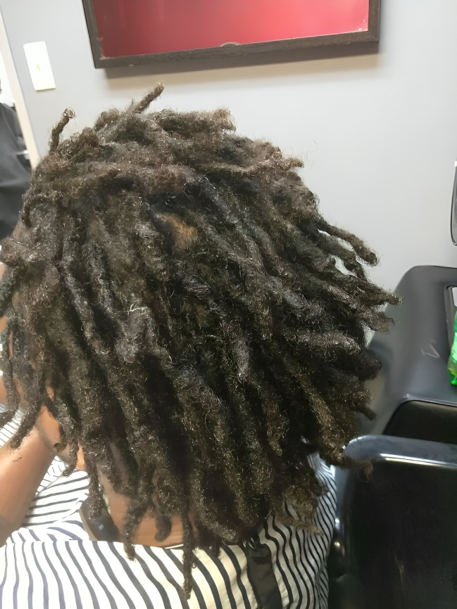 A man with dreadlocks is sitting in a chair in a salon.