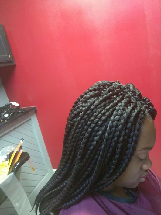 A woman with braids is sitting in front of a red wall