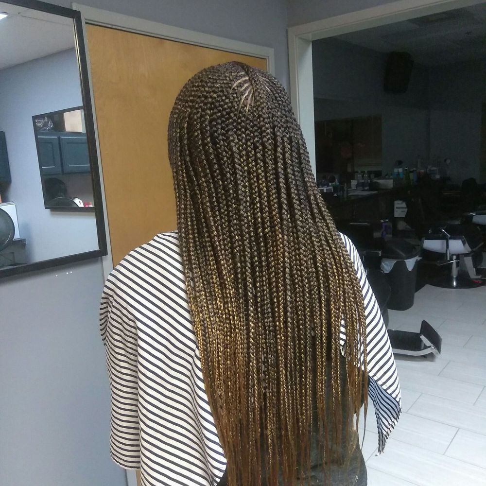 A woman with braids is standing in front of a mirror in a room.