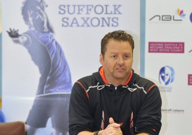 A man sitting in front of a sign that says suffolk saxons