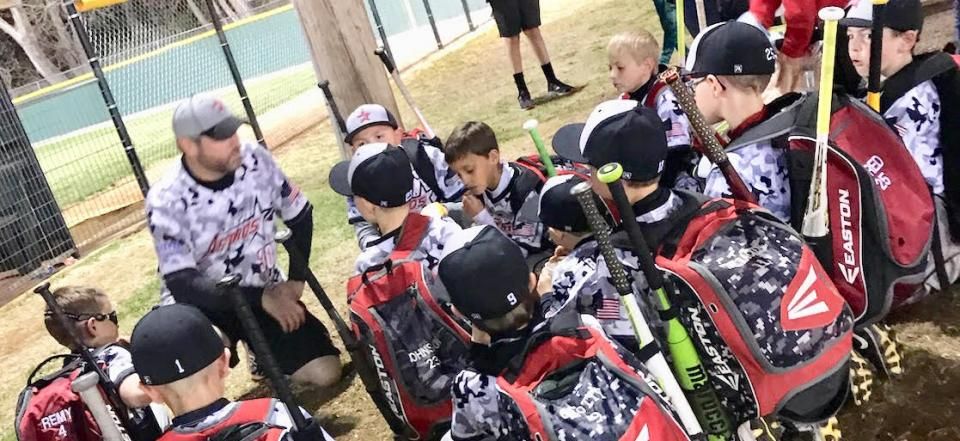 Children with baseball gear seated on a bench, listening to a coach during a game or practice.