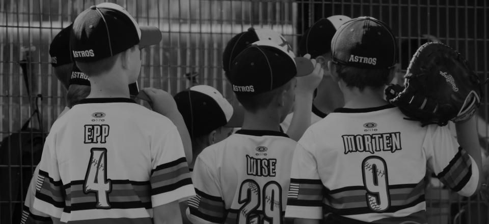 Three young baseball players in black-and-white uniforms standing together, seen from behind with jersey numbers.